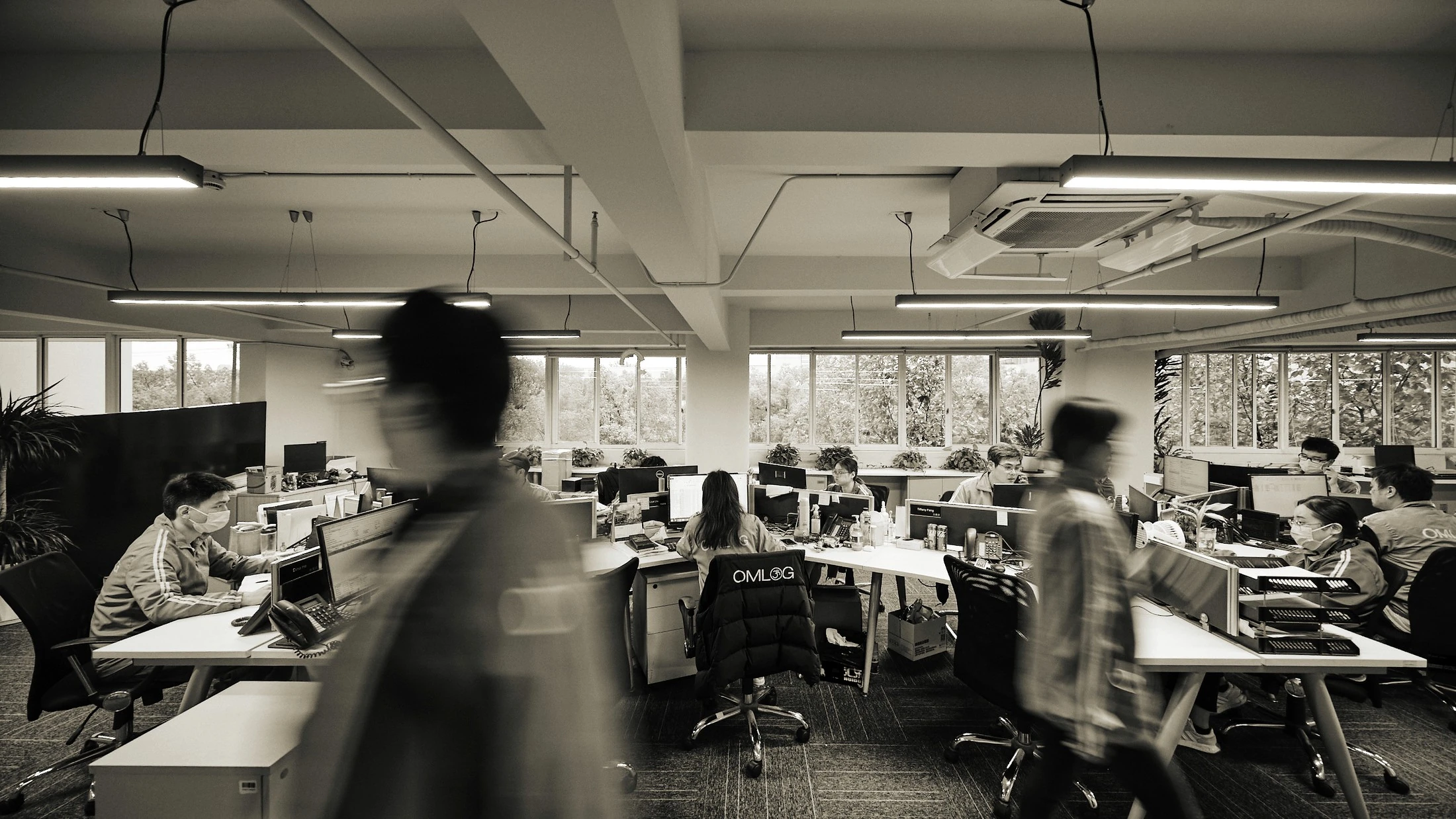 Open-plan office with consultants at their workstations, motion blur of people moving through the foreground, black and white