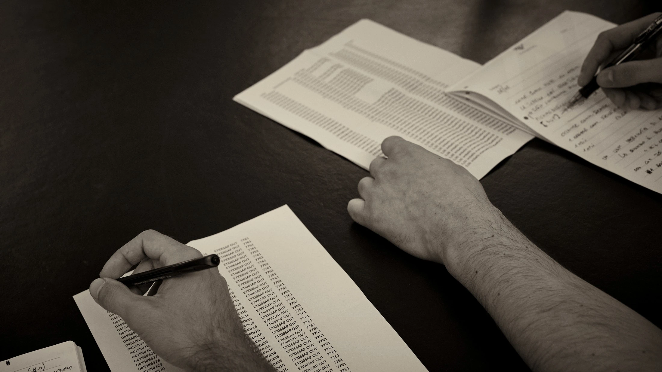 Close-up of hands annotating a printed shipment report during an analysis session, black and white