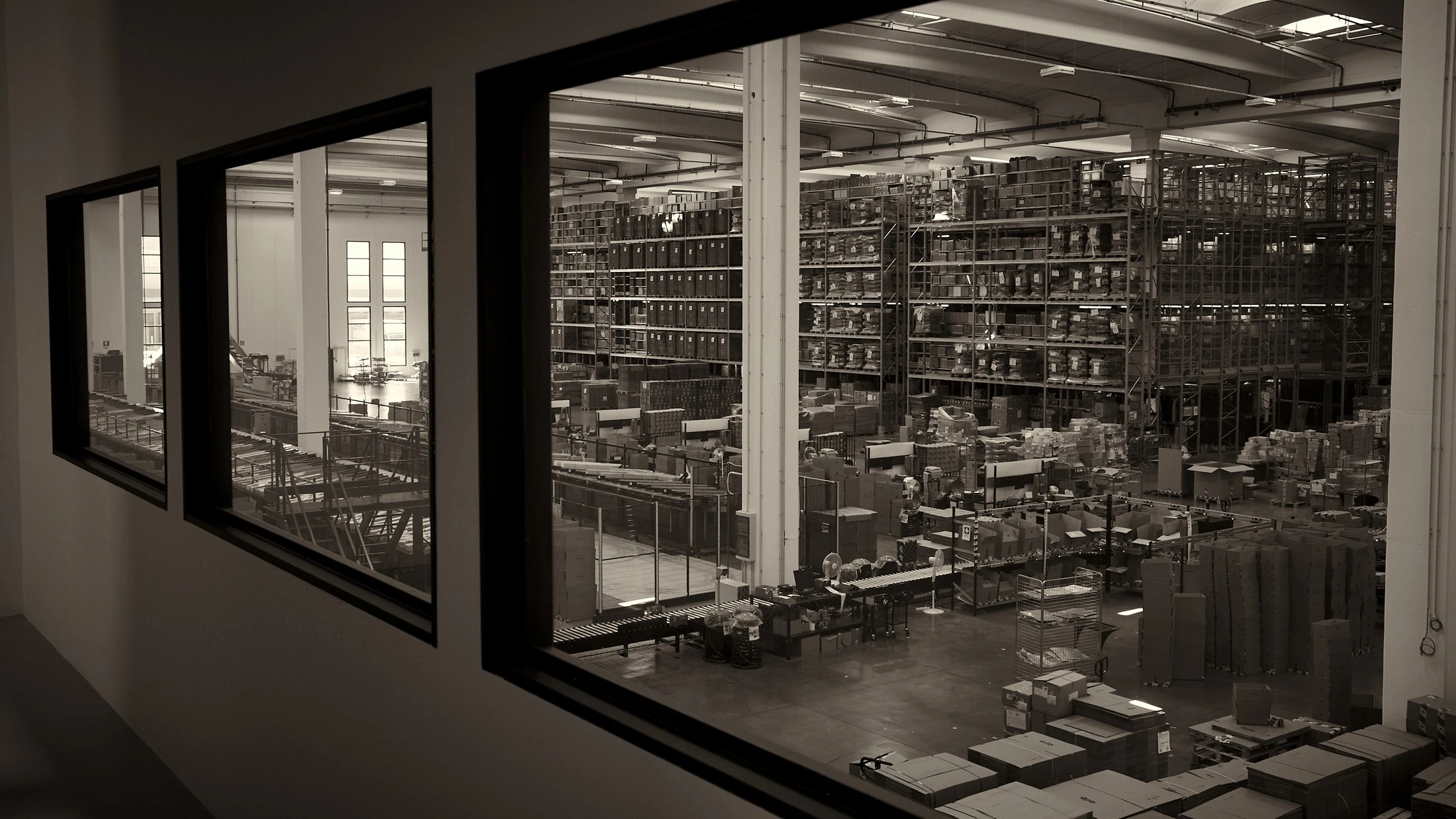 Elevated view over a full warehouse floor with racking and sorting lines, black and white