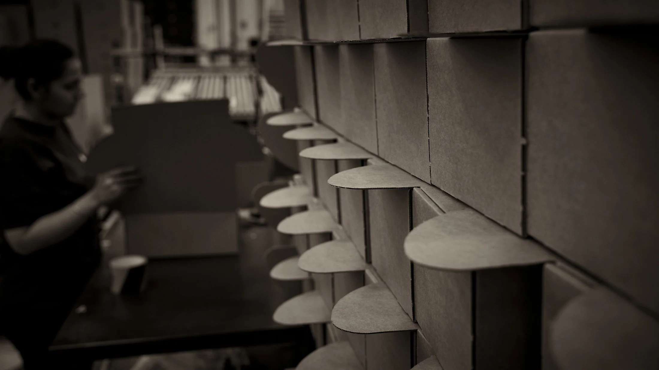 Fan of cardboard divider files stacked on a shelf, with a blurred operator at a workbench in the background