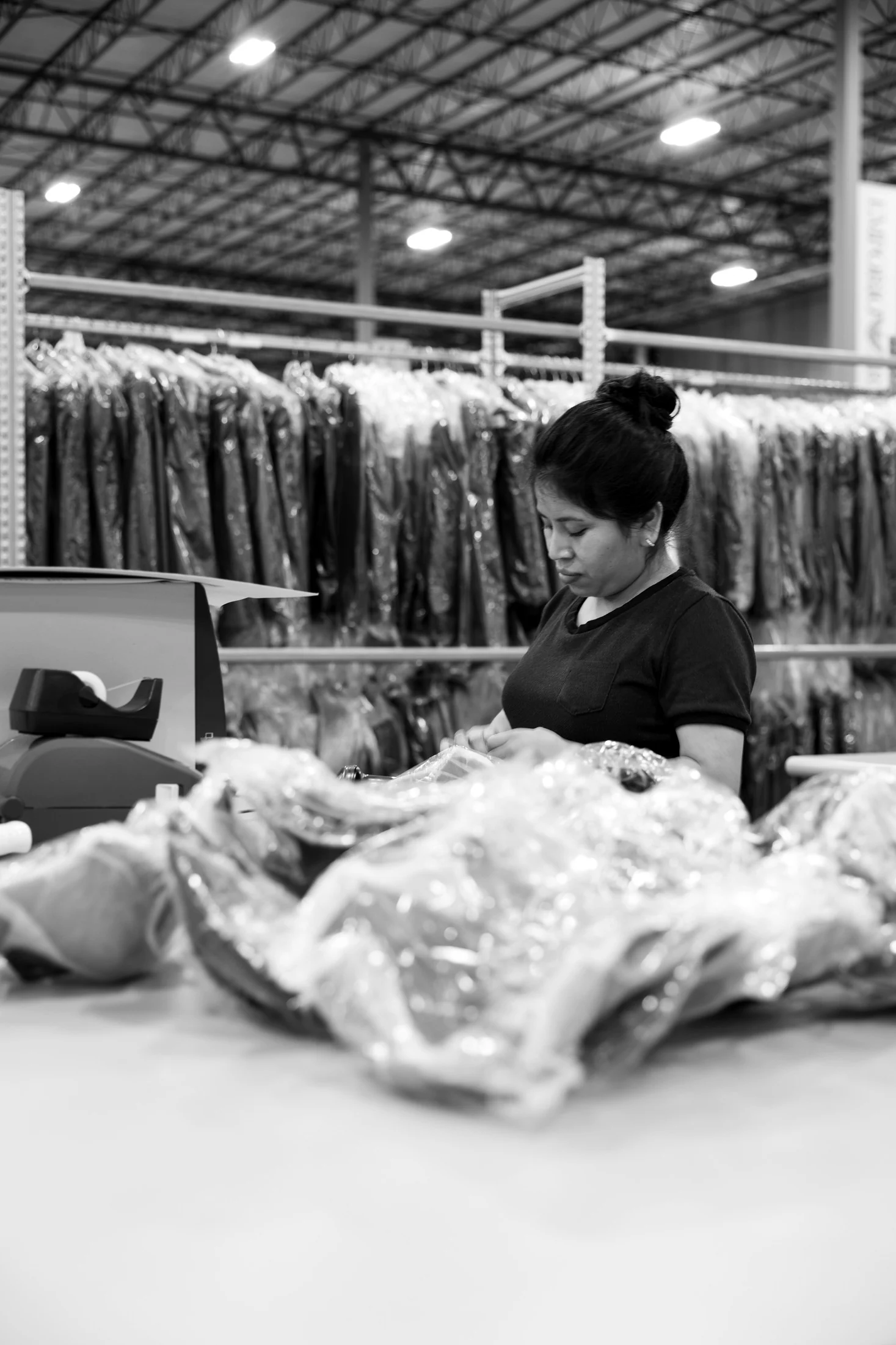 Operator wrapping a garment by hand in protective film in front of a rack of bagged garments