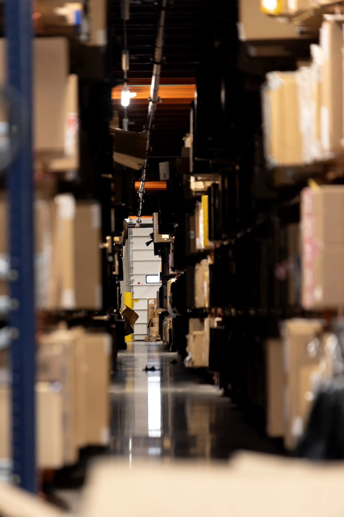Dark corridor between box shelving with a deep perspective toward a sorting doorway at the far end