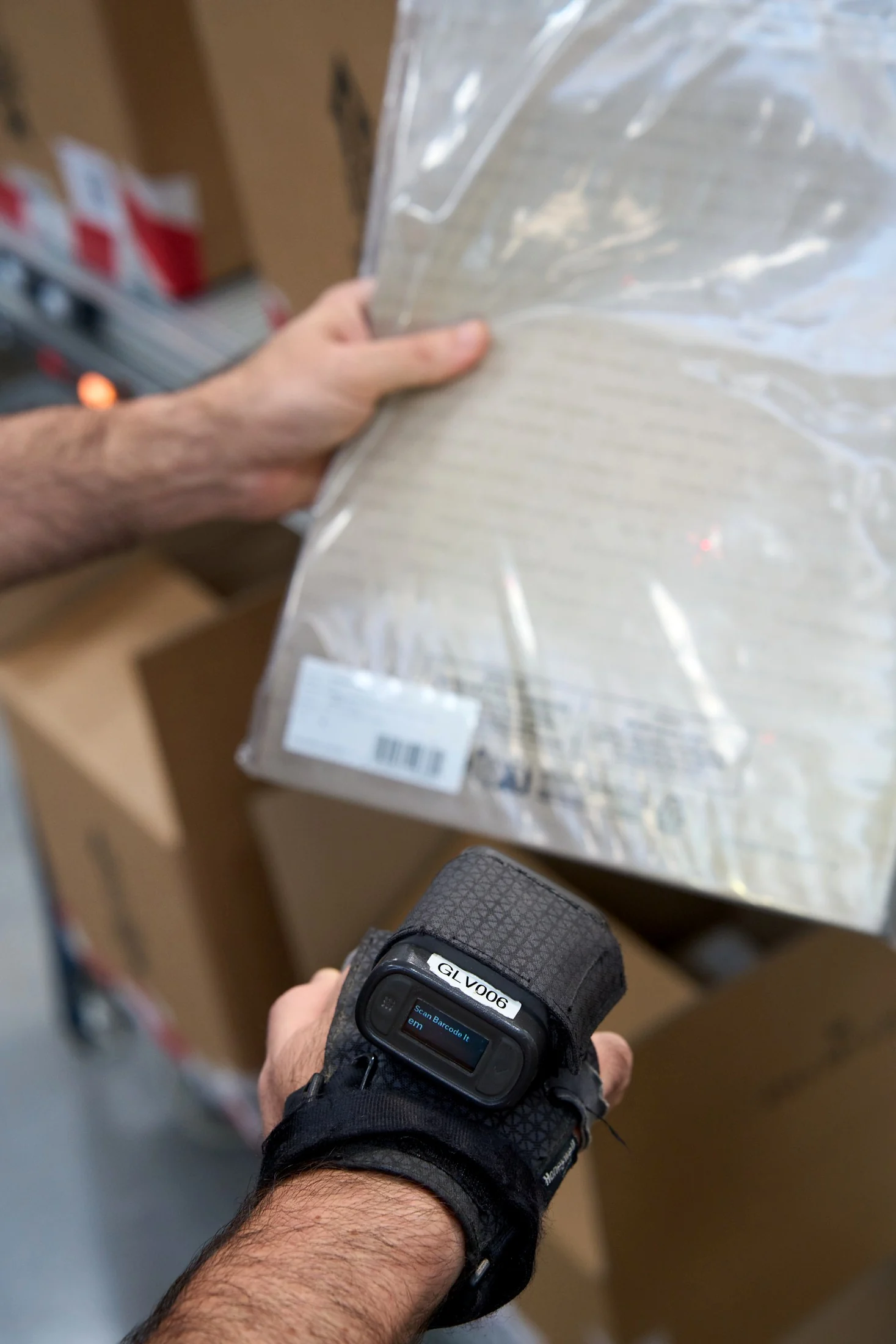 Operator scans a wrist mounted barcode reader against a poly bagged garment under warehouse lighting