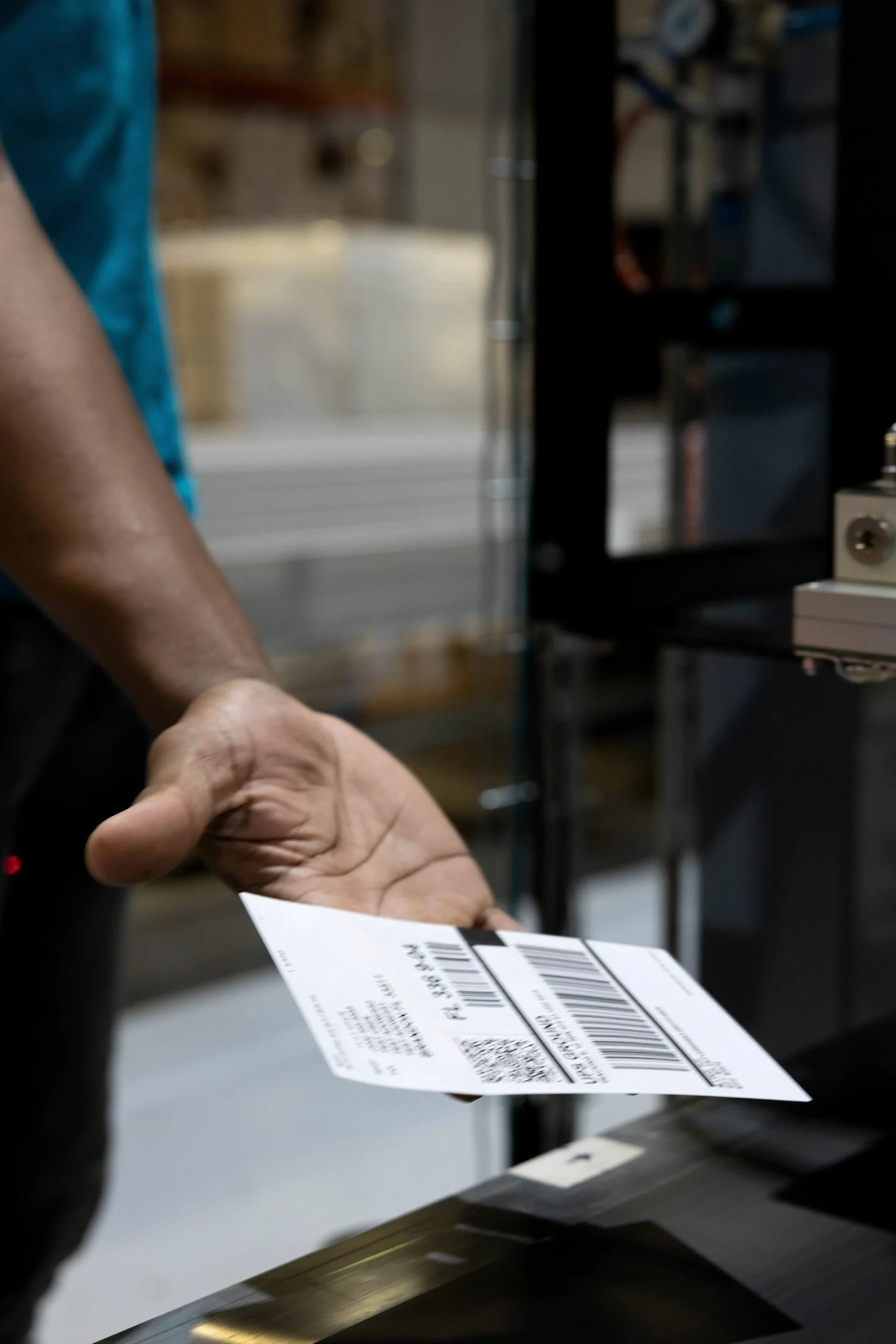 Hand holding out a shipping label with barcode and QR code towards the camera, warehouse blurred behind