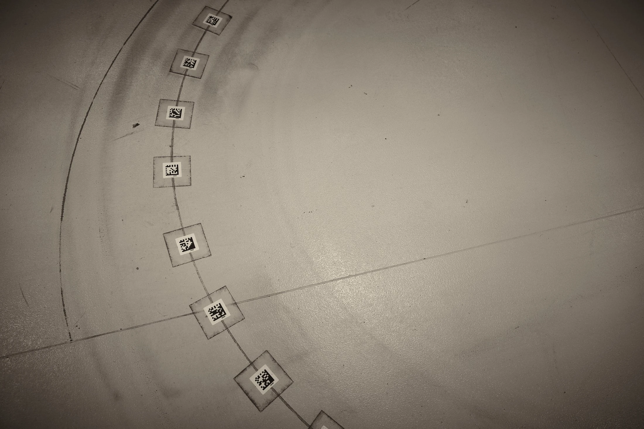 Overhead view of coded QR floor markers guiding automated robot navigation in a group warehouse, black and white