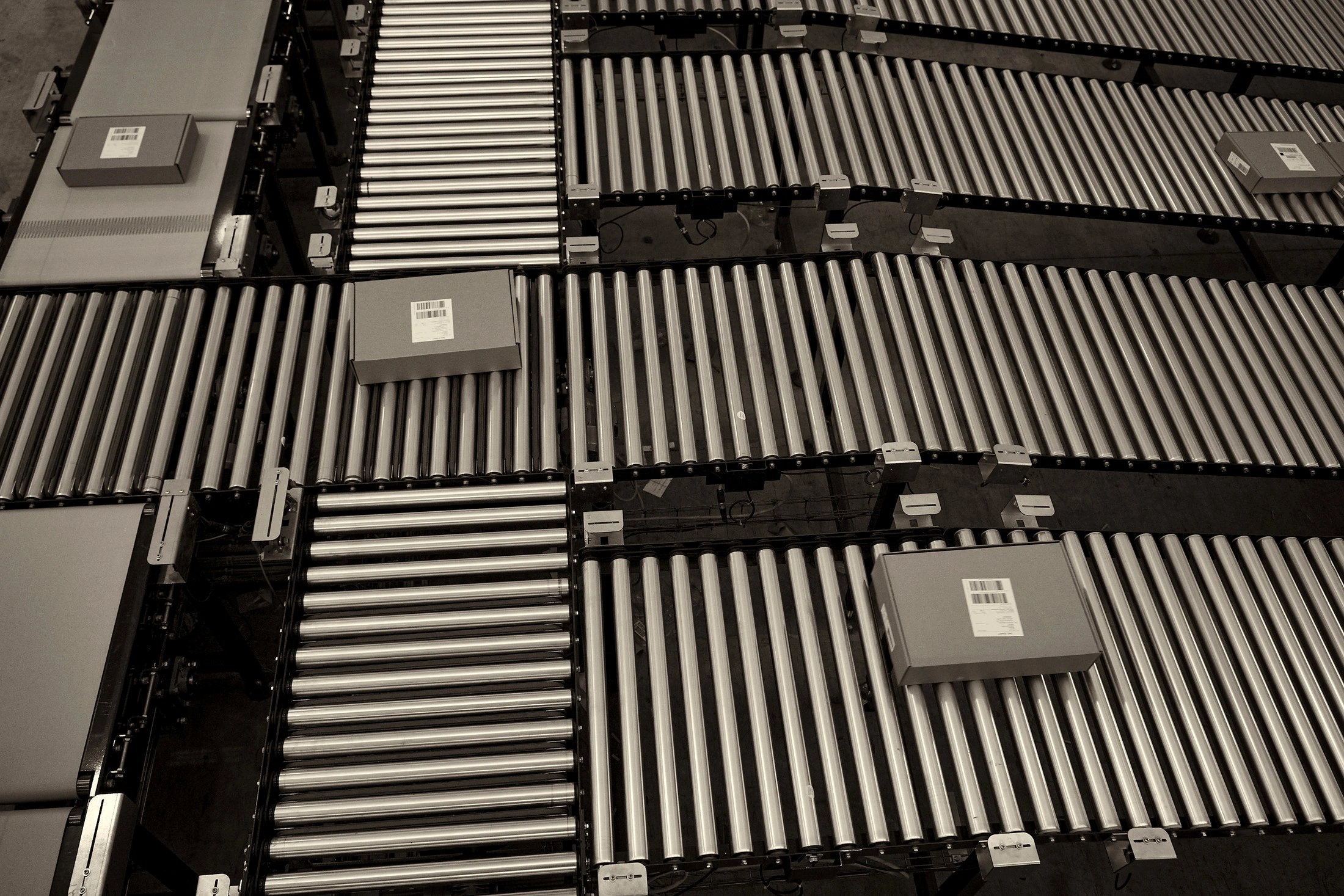 Overhead black and white view of roller conveyors carrying parcels with barcode labels through a group distribution centre